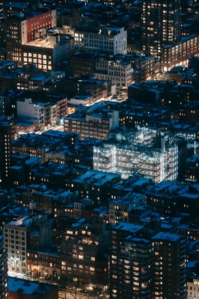 From above of contemporary residential tall buildings with glowing lights located on street of modern megapolis at dark night time