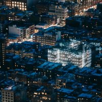 From above of contemporary residential tall buildings with glowing lights located on street of modern megapolis at dark night time